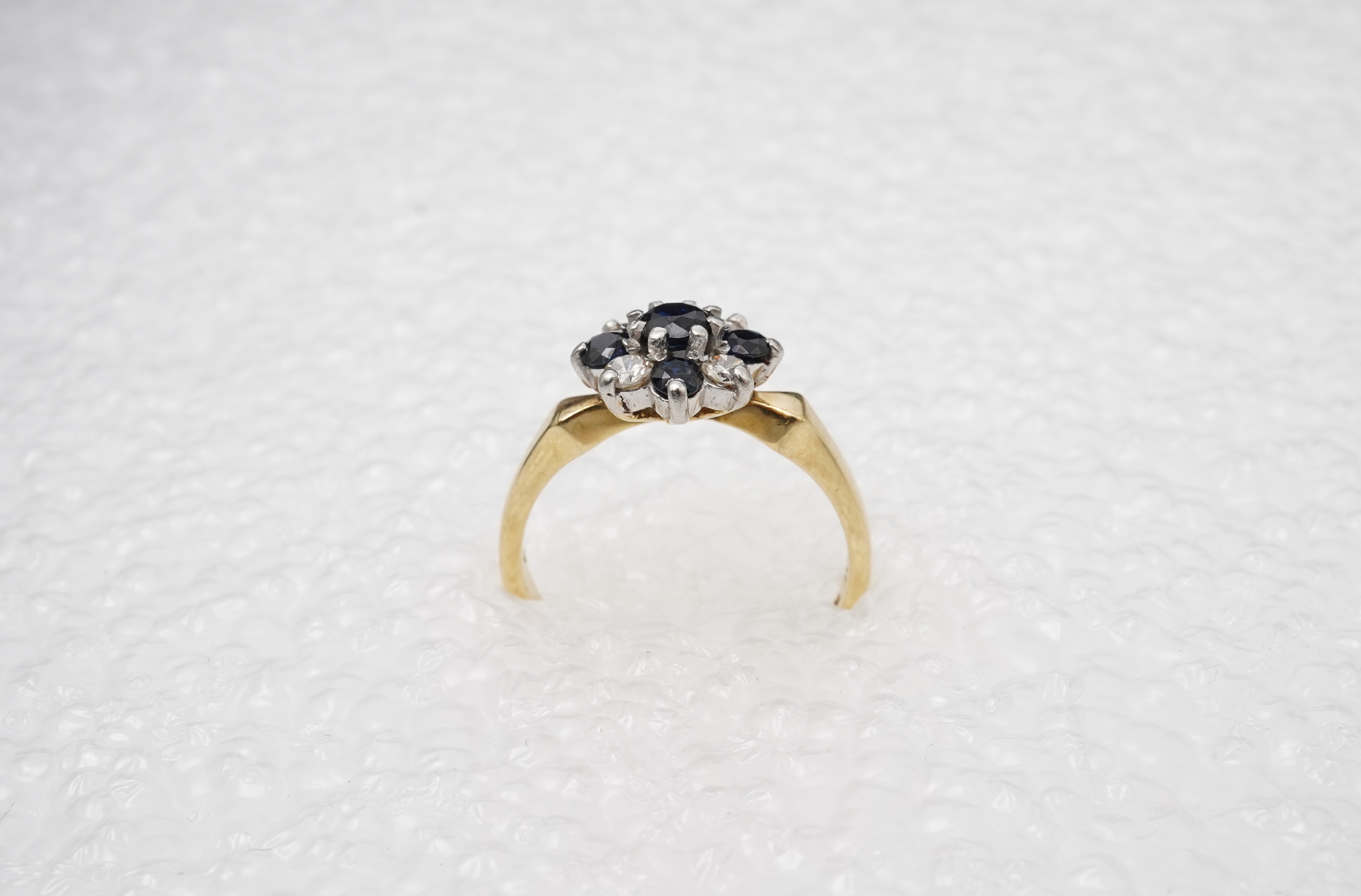 A sapphire and diamond cluster ring, set with circular-cut sapphires and brilliant-cut diamonds totalling approximately 0.20 carats, mounted in gold and platinum, size M, stamped 18CT PLAT, gross weight approximately 3.5